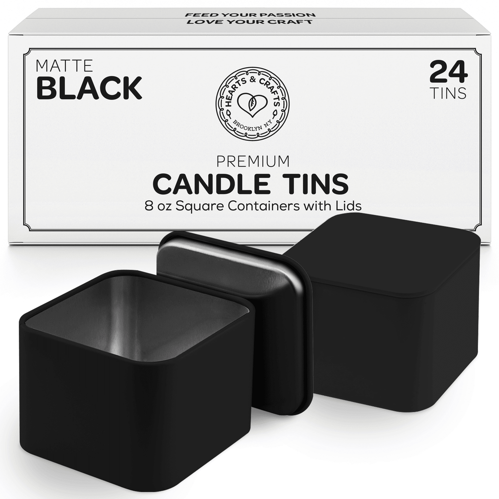 Two square black candle tins with lids in front of white box packaging on a white background - closeup view