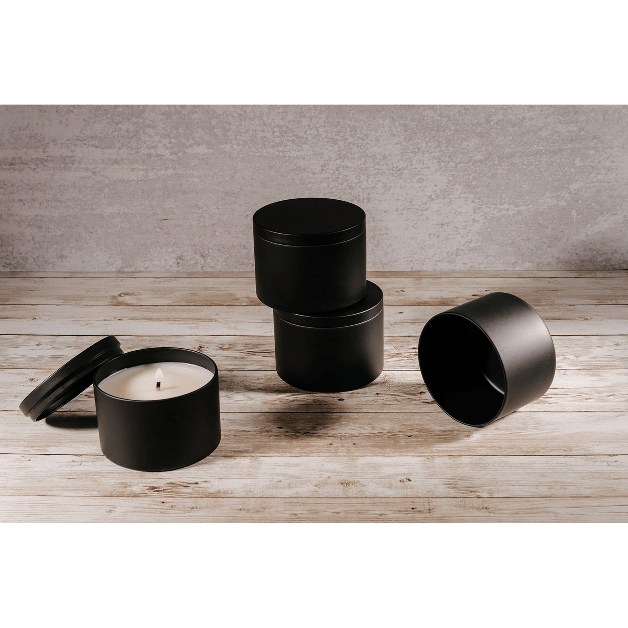 Four black cylindrical containers with lids and a candle on a wooden surface