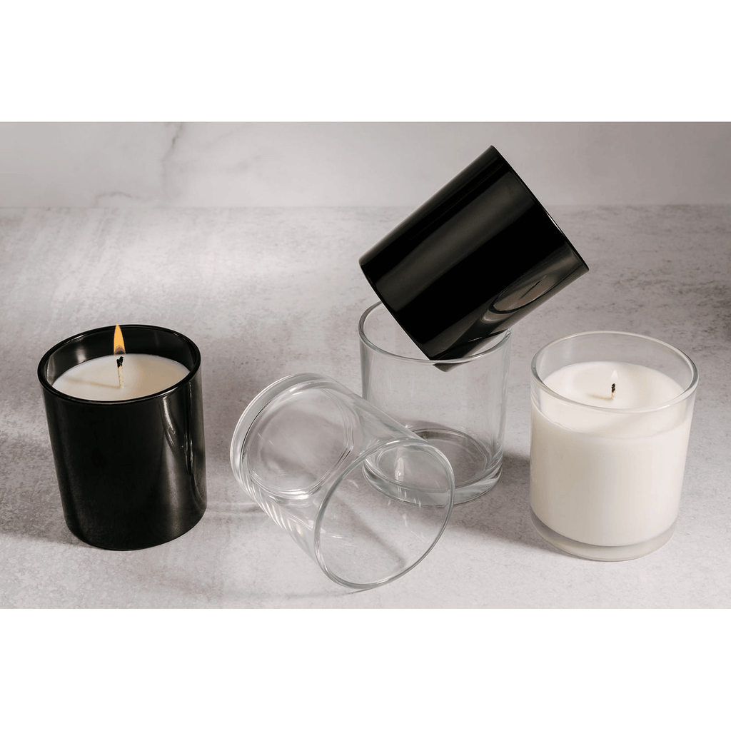 Black and clear glass candle holders with lit white candles on a light gray surface