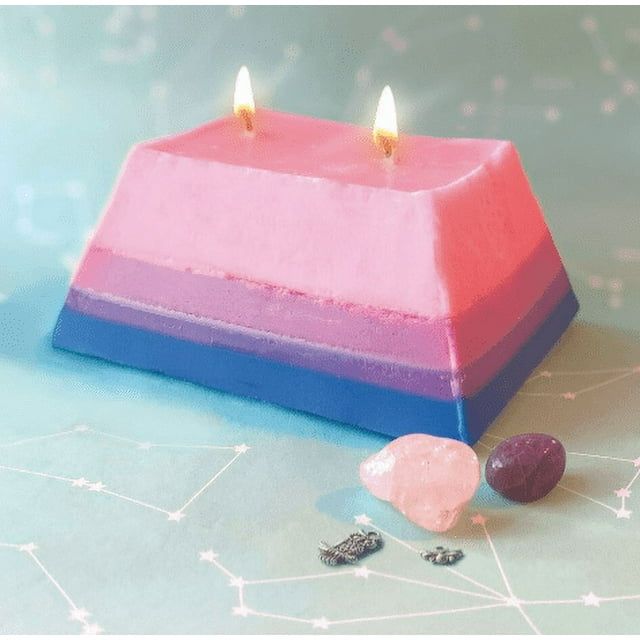 Triangular pyramid candle with two lit wicks and gemstones in front on light blue background with constellations - DIY treasure candle