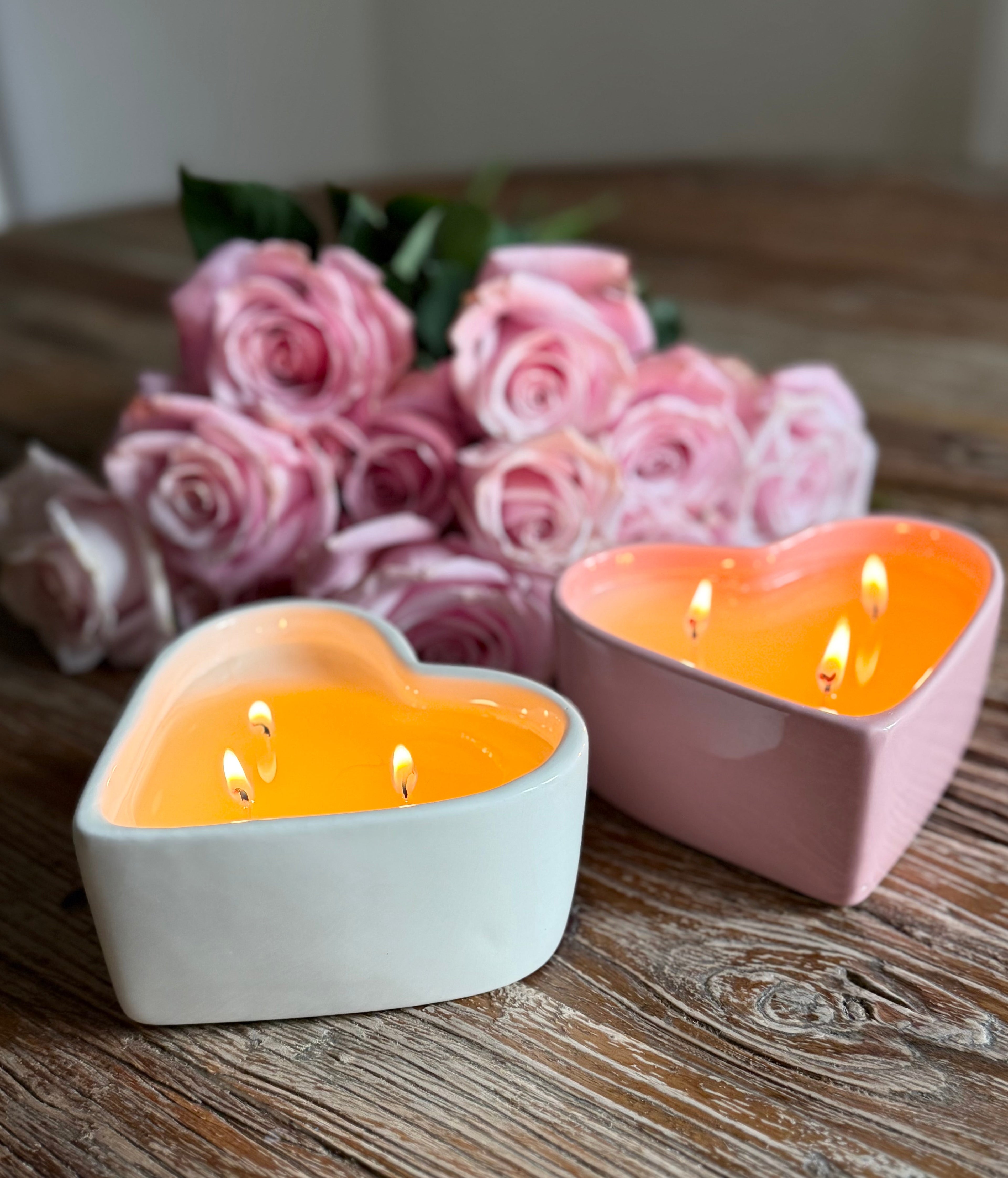Close-up of pink and white heart-shaped candles with three lit wicks on wooden surface with pink roses - Valentine's Day ceramic candle