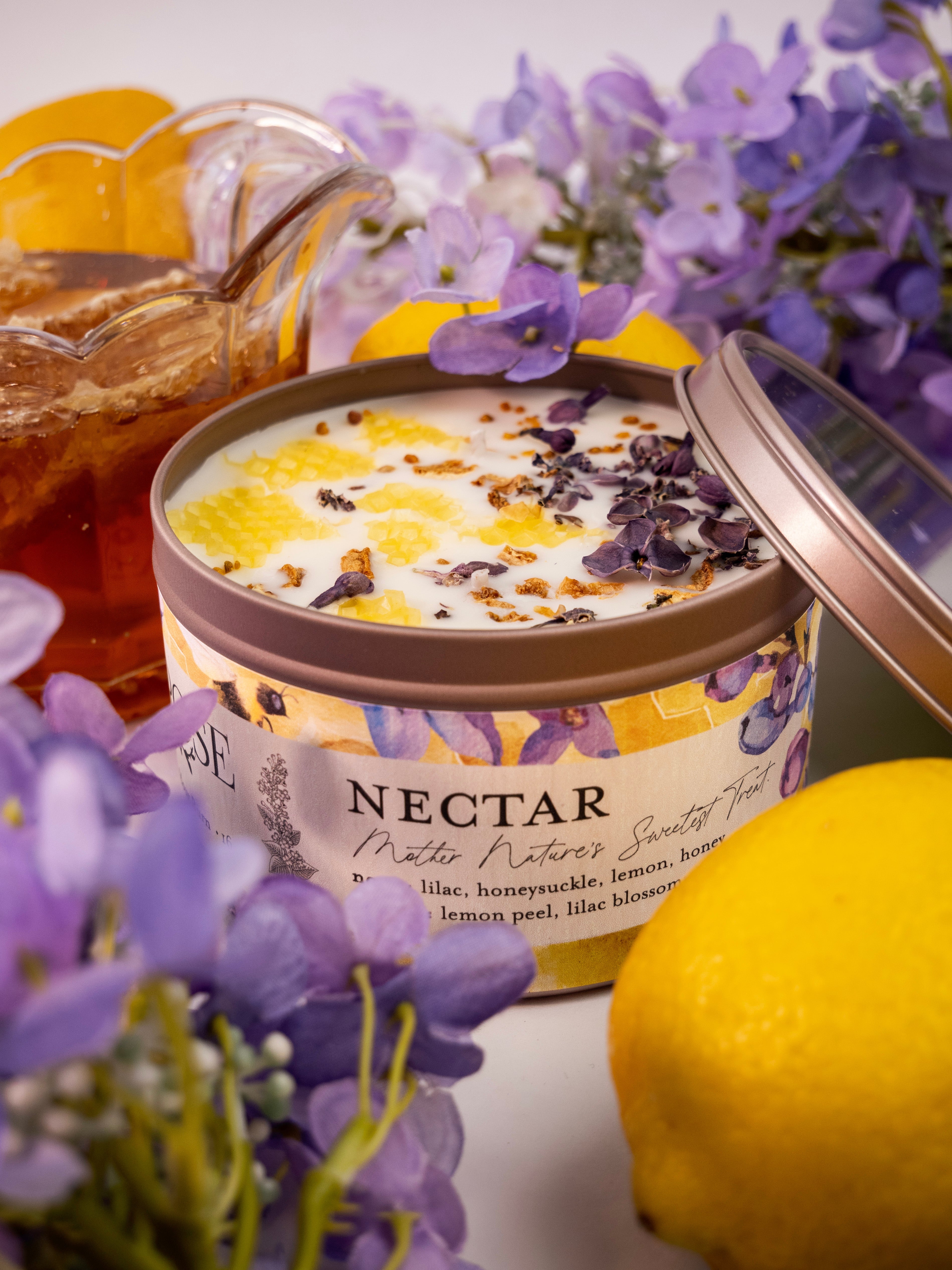 Front view of NECTAR candle tin with lid off surrounded by lemons and flowers on white background - closeup