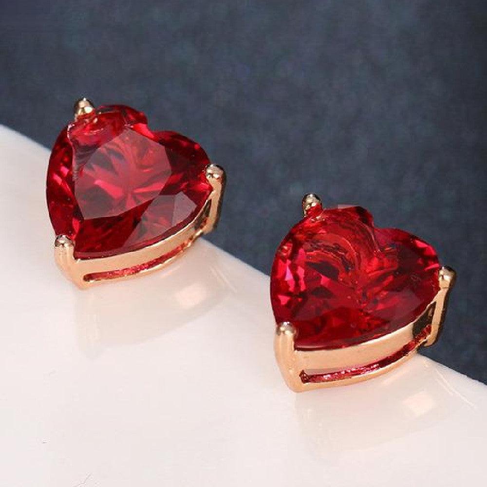 Red heart-shaped water diamond gemstone earrings with rose gold accents on white surface with dark background for Valentine's Day