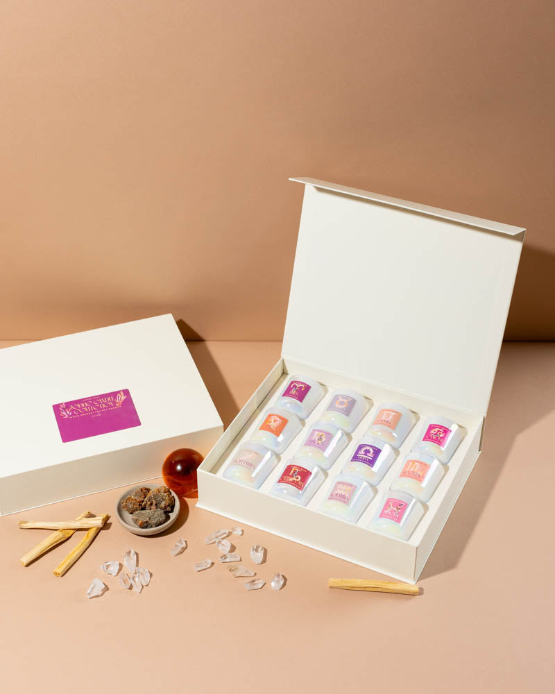 Open white magnetic candle box with pink label containing 12 colorful labeled 2.5oz candles on beige background - large candle sampler packaging