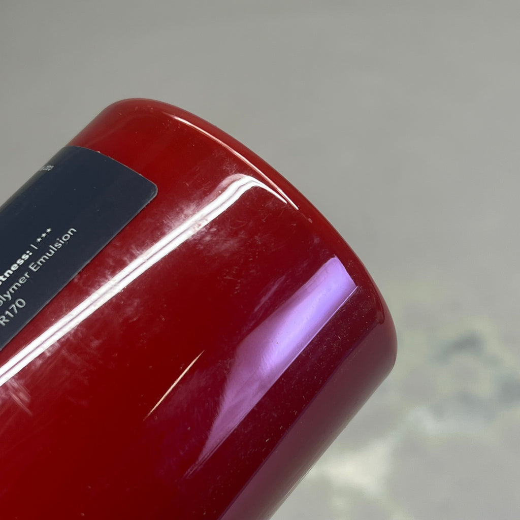 Bottom view of Master's Touch Crimson acrylic paint bottle showing red paint color through transparent plastic container on gray background - bottle base detail