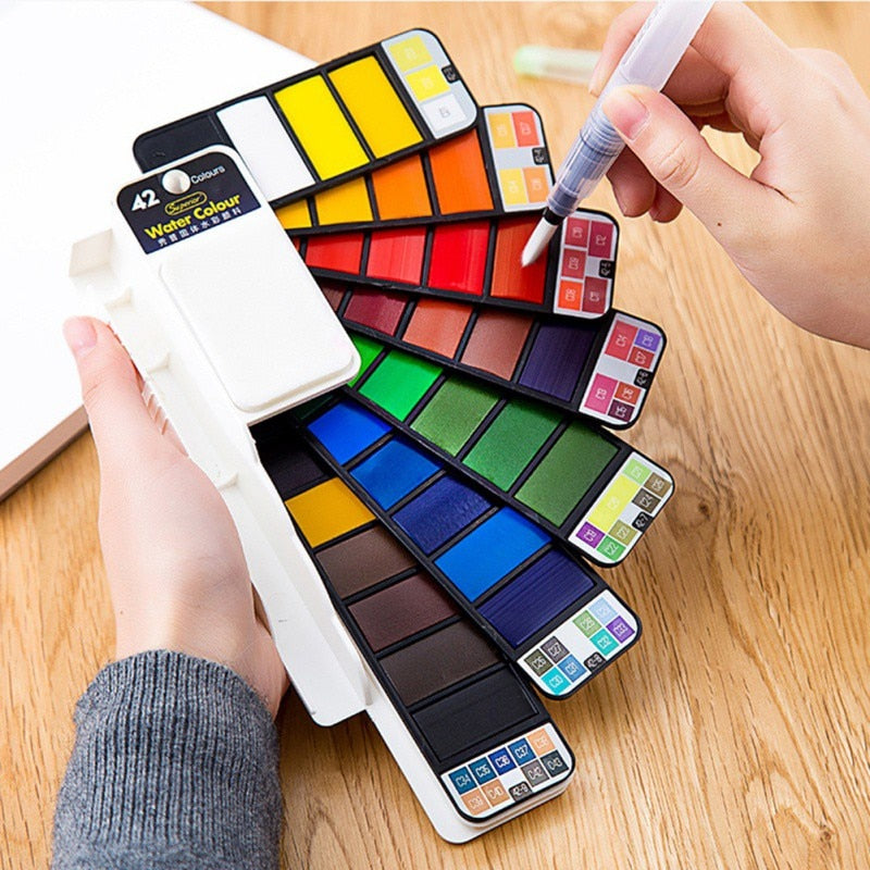 Professional watercolor paint pans with hand holding water brush on wooden surface - foldable watercolor painting set