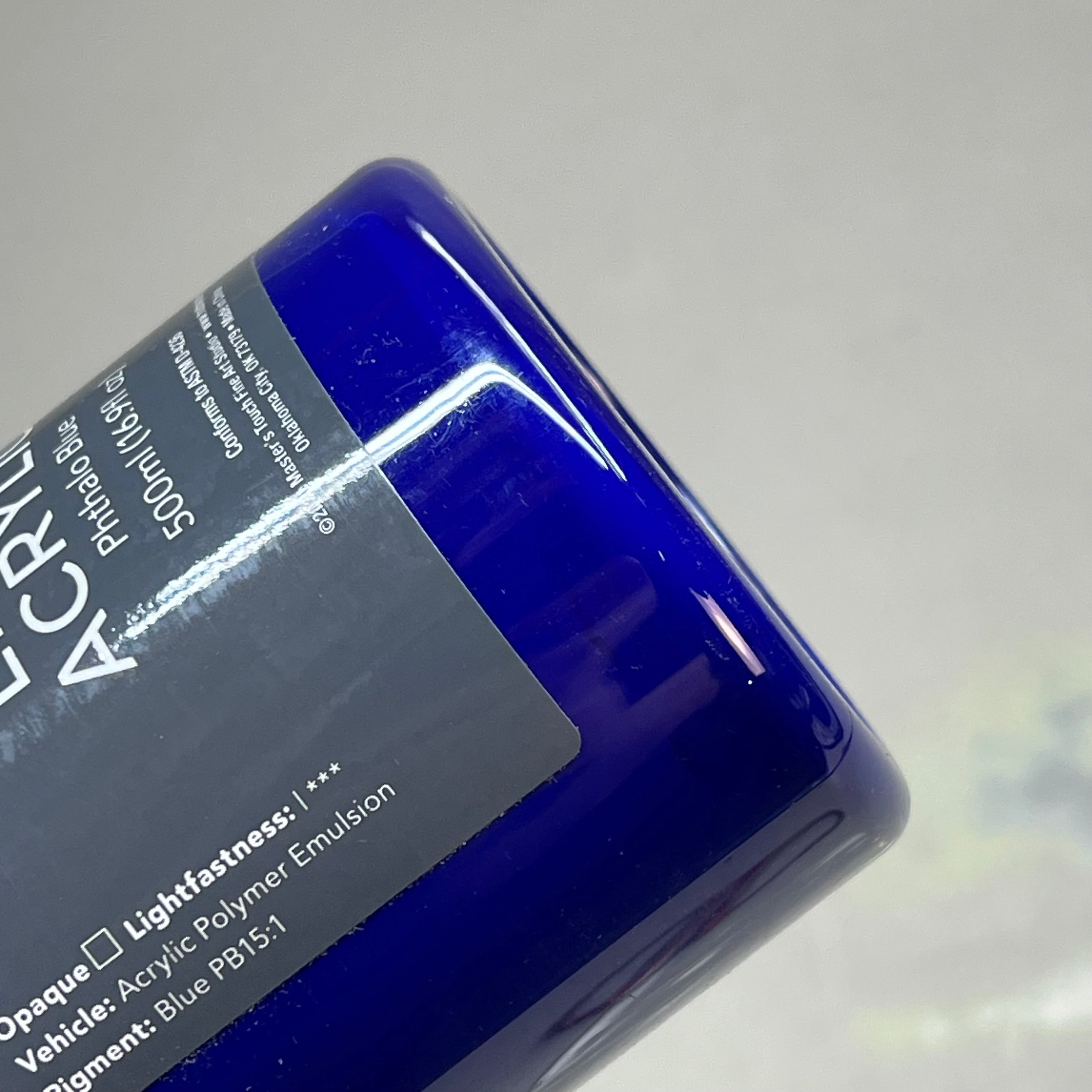 Upside down bottom view of Master's Touch Phthalo Blue acrylic paint bottle showing dark blue paint color through transparent plastic container with label on gray background