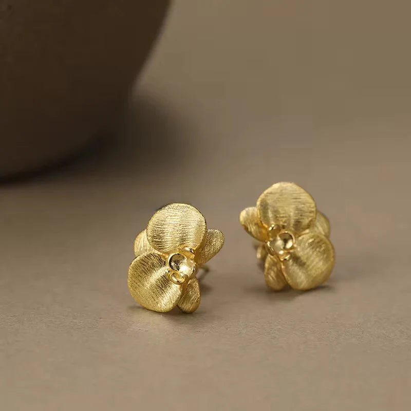 Pair of gold orchid flower stud earrings on brown background - 18K gold plated