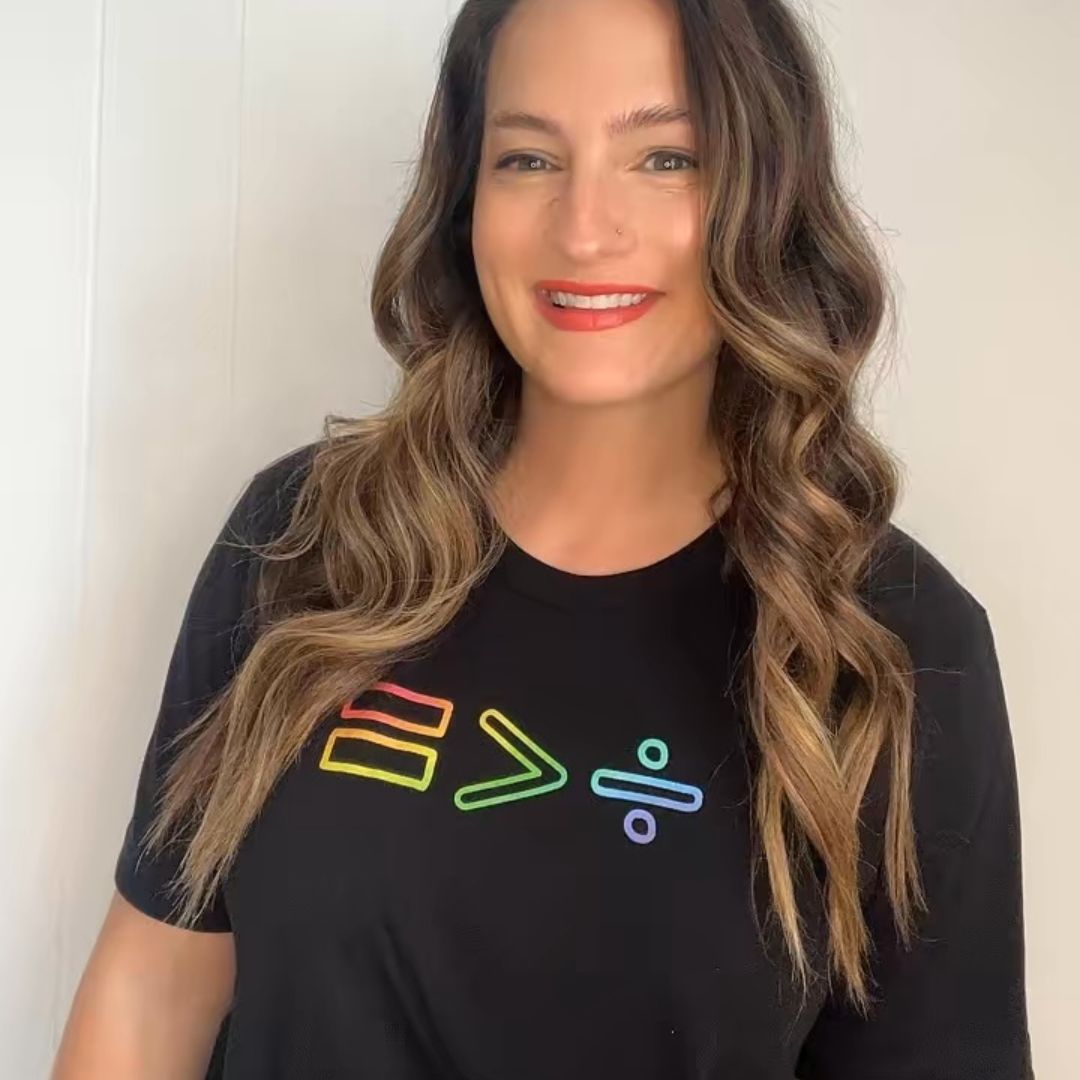 Woman wearing black unisex t-shirt with colorful equality greater than division symbols on plain background