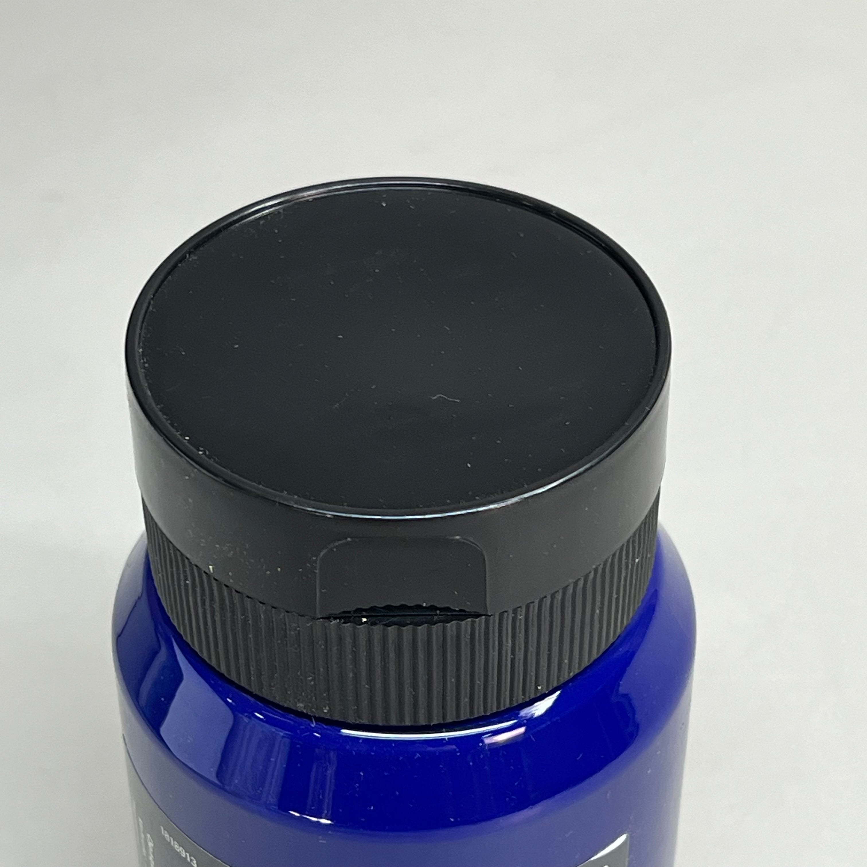 Close-up top view of Master's Touch Phthalo Blue acrylic paint bottle with black lid showing dark blue paint color through transparent plastic container on white background