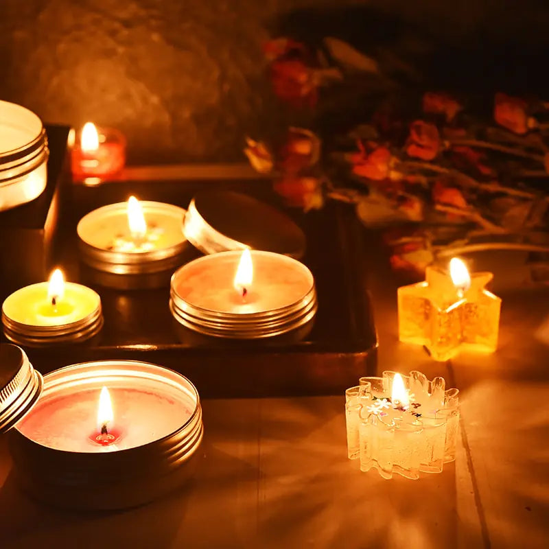 Lit candles in various holders on reflective surface with dark background