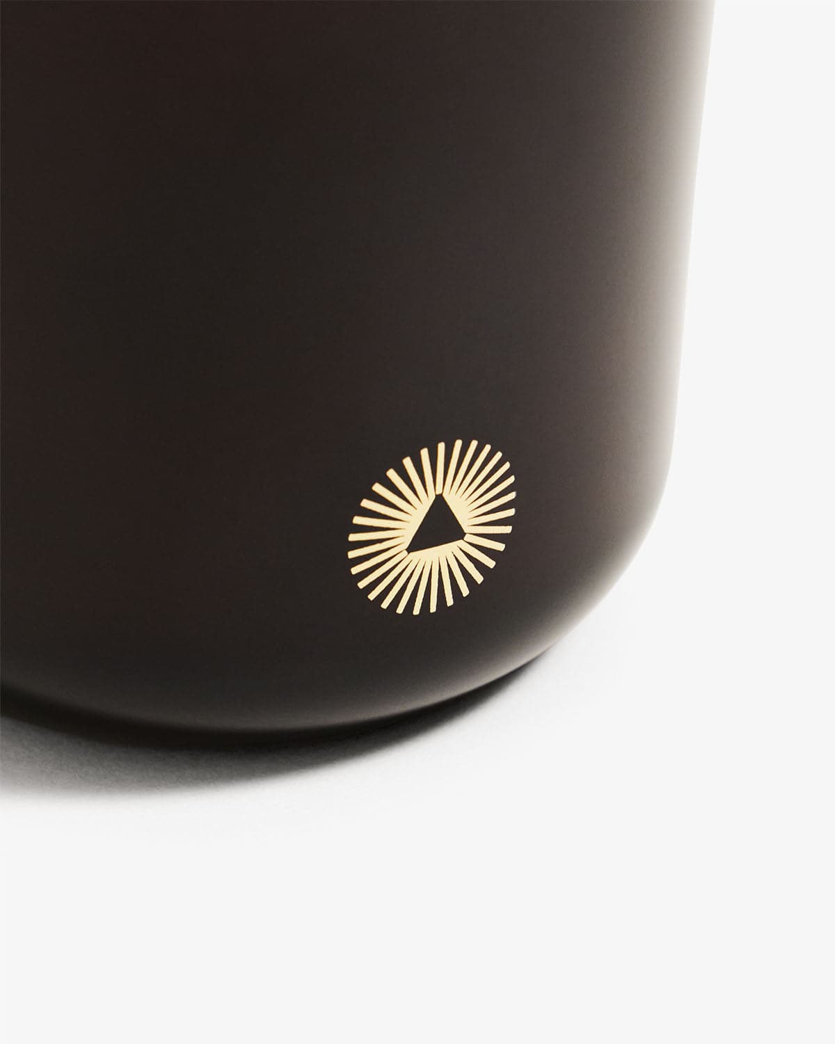 Close-up of black Grateful candle container bottom with gold pyramid logo - back view of aromatherapy candle packaging
