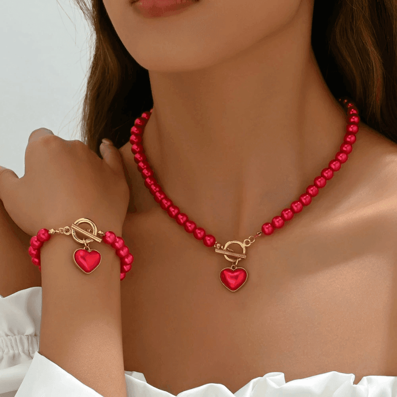 Close-up of red beaded necklace and bracelet with heart charms worn on person in white top showing Valentine's Day jewelry set
