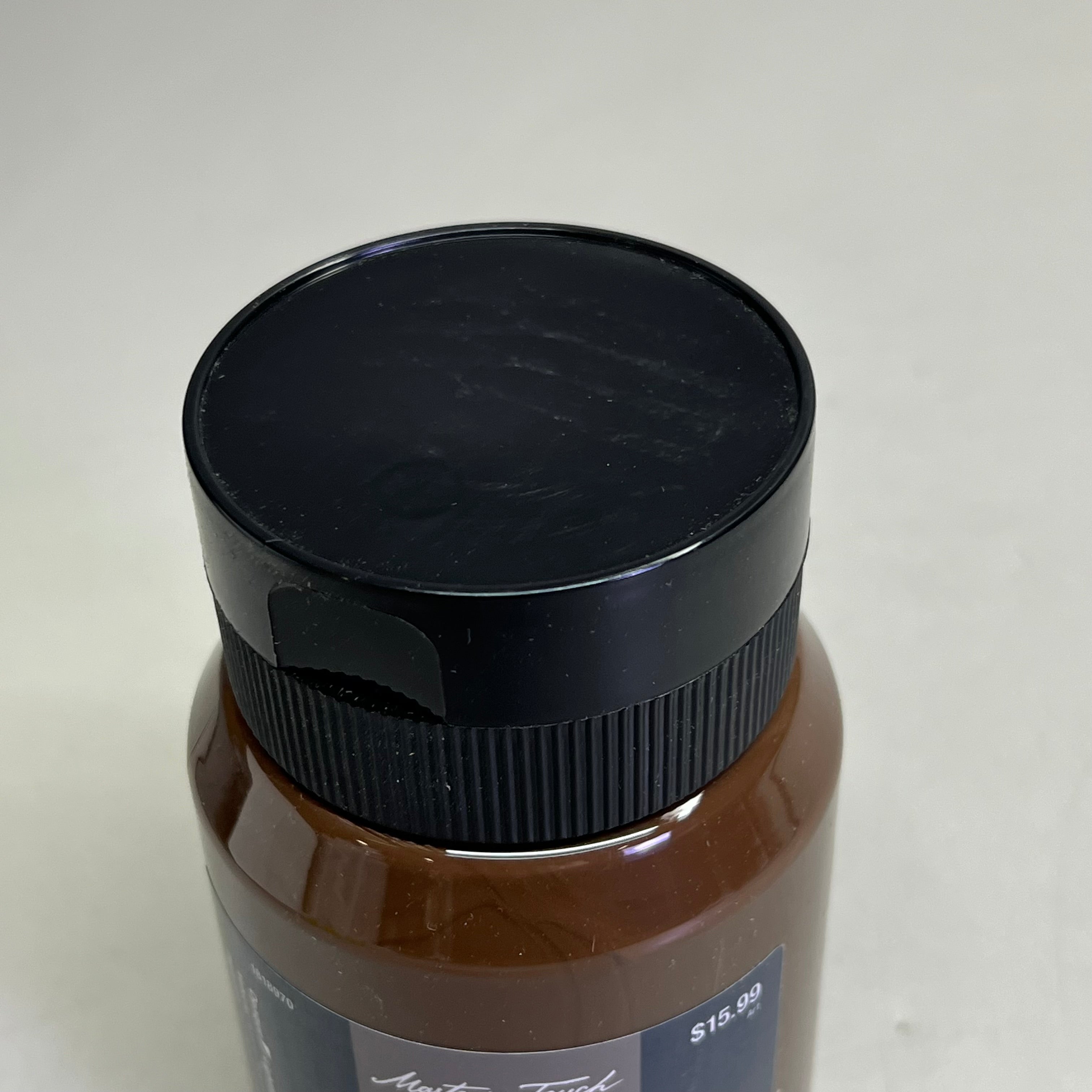 Close up of black bottle cap on Master's Touch raw umber acrylic paint bottle on white background