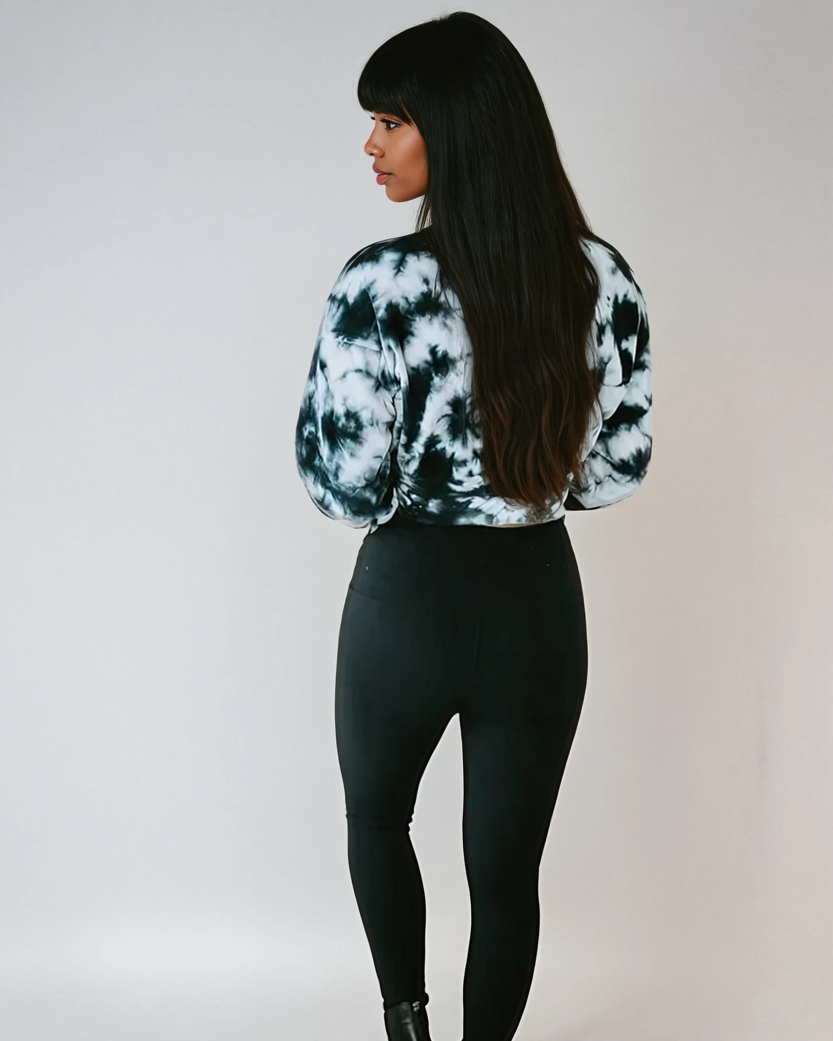 Woman wearing black and white tie-dye crop pullover and black pants against plain background - back view athleisure top
