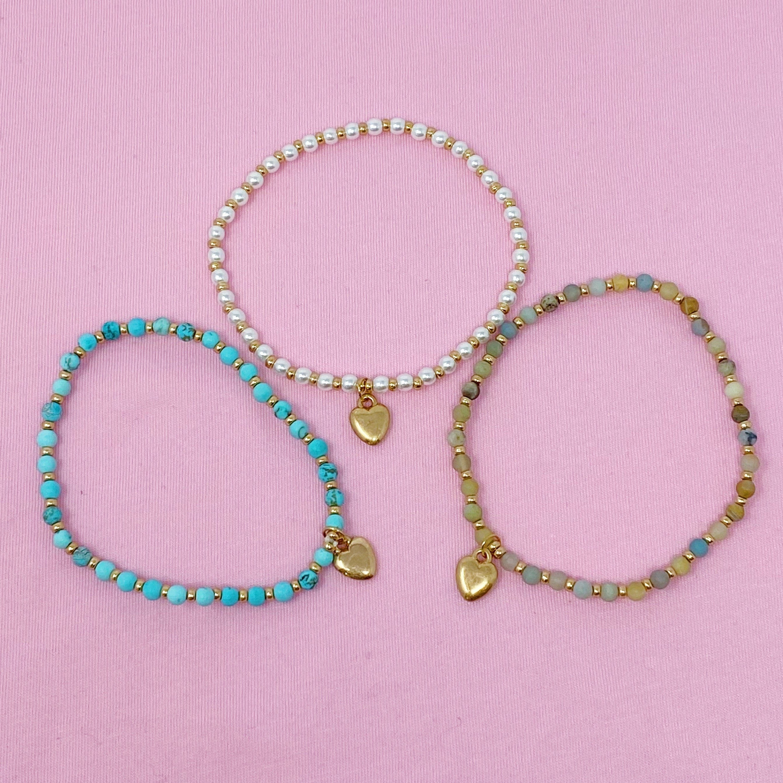 Three stone bead heart anklets with gold charms - pearl, turquoise, and amazonite on pink background - Valentine's Day jewelry