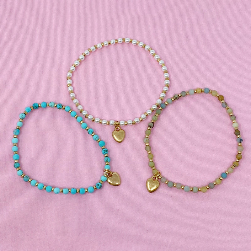 Three stone bead heart anklets with gold charms - pearl, turquoise, and amazonite on pink background - Valentine's Day jewelry