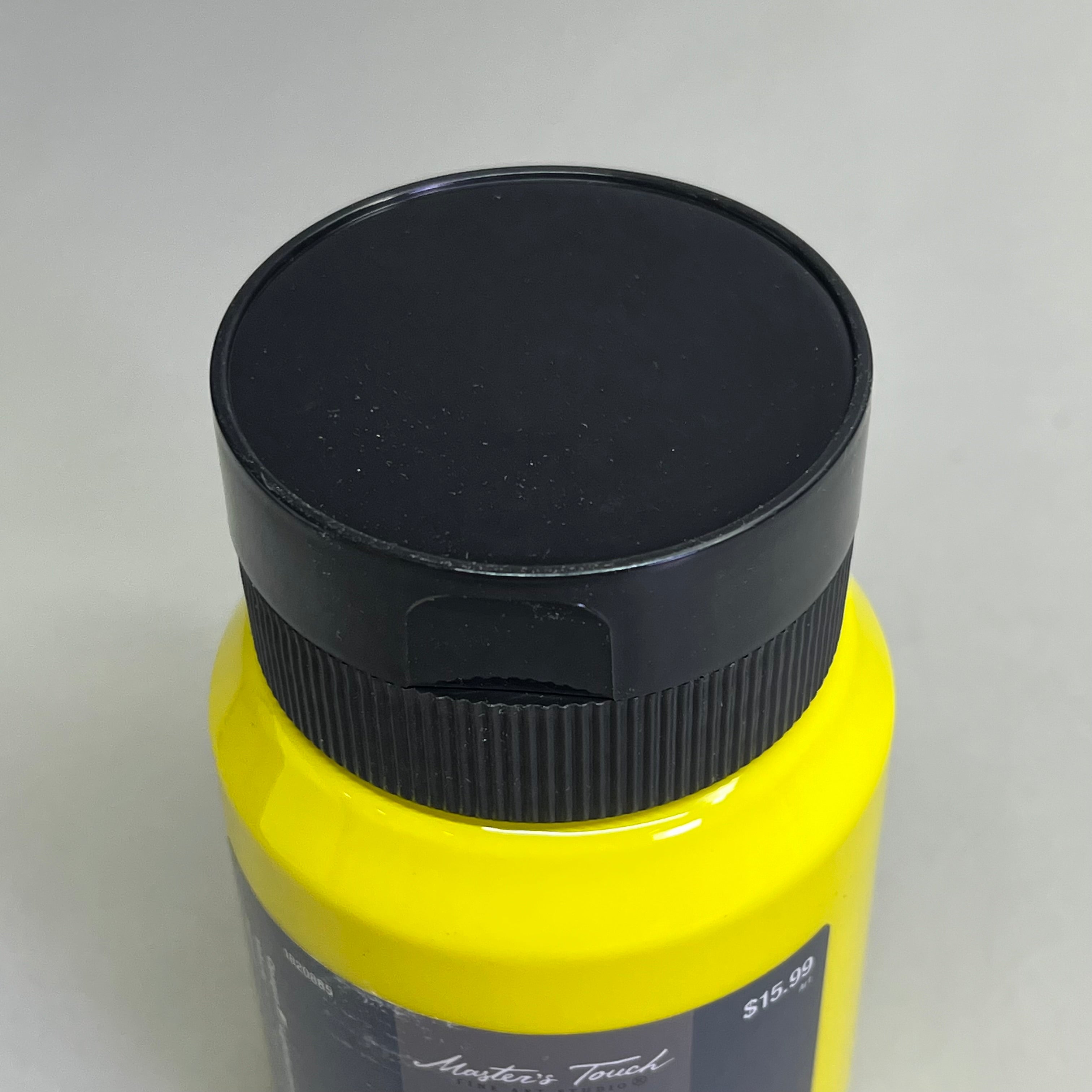 Close up of black bottle cap on Master's Touch lemon yellow acrylic paint bottle on white background