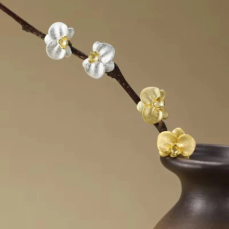 Decorative branch with gold and silver orchid stud earrings on brown background - closeup view