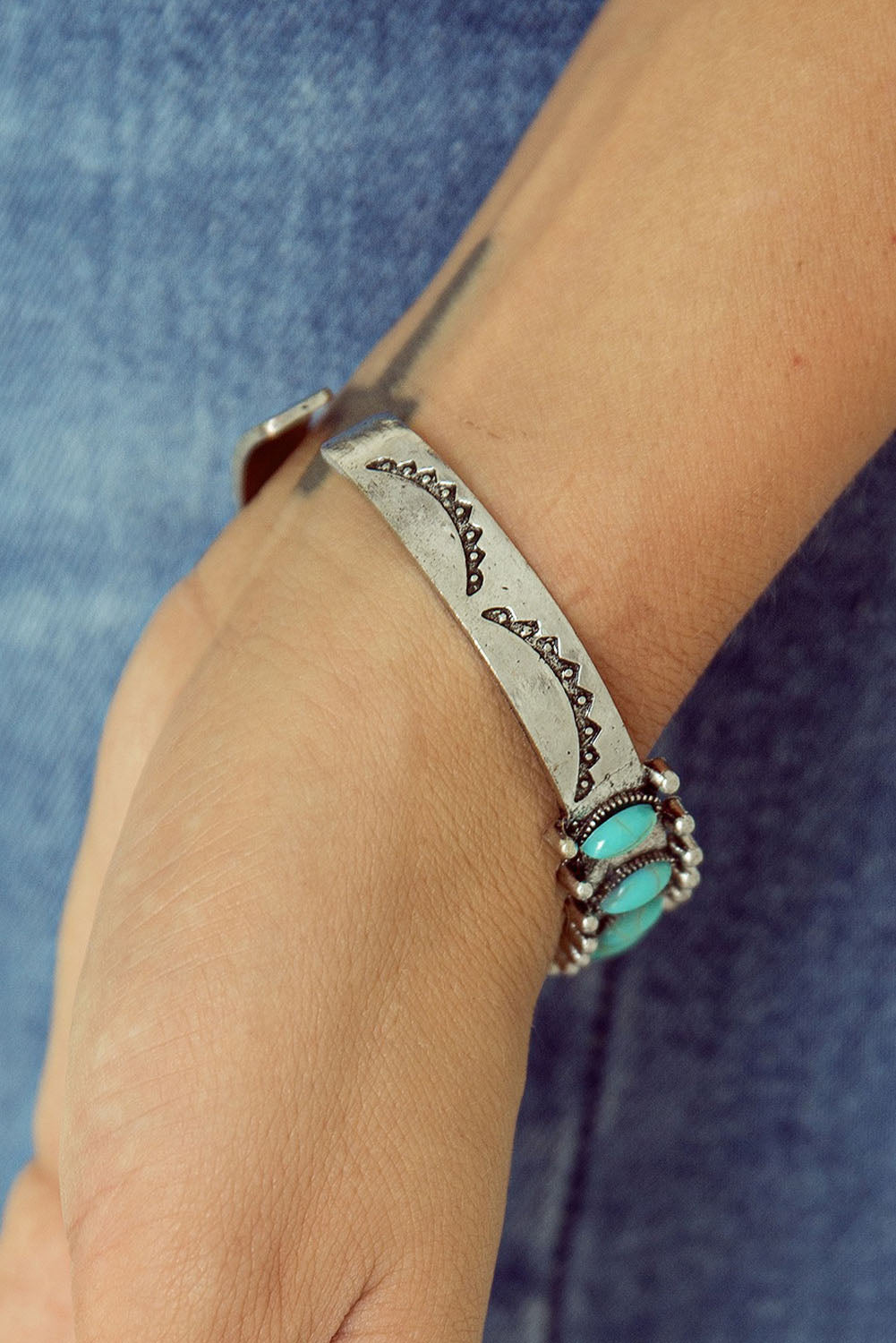 Silver cuff bracelet with turquoise stone on wrist - side view showing embossed design detail