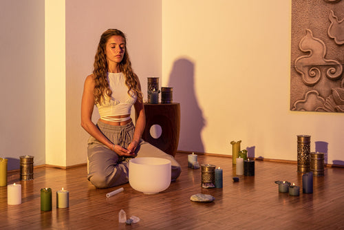 Woman in meditation with white crystal singing bowl and candles during sacral chakra healing session creating serene atmosphere