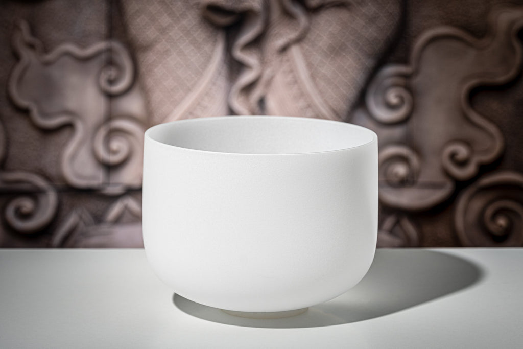 White frosted crystal singing bowl on reflective surface with decorative brown background showing pure quartz quality