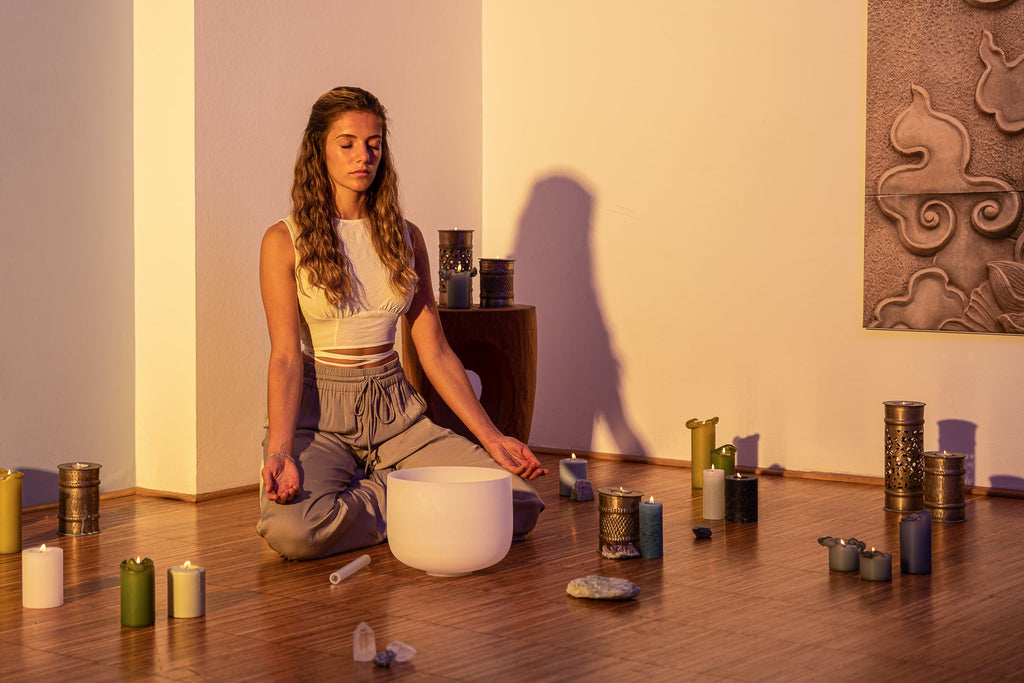 Woman in meditative pose with white crystal singing bowl and candles during heart chakra healing session