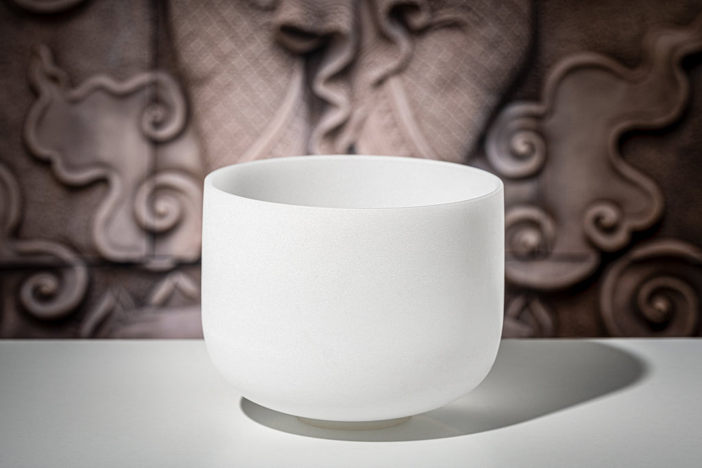 White frosted crystal singing bowl on reflective surface with textured brown background showing pure quartz quality