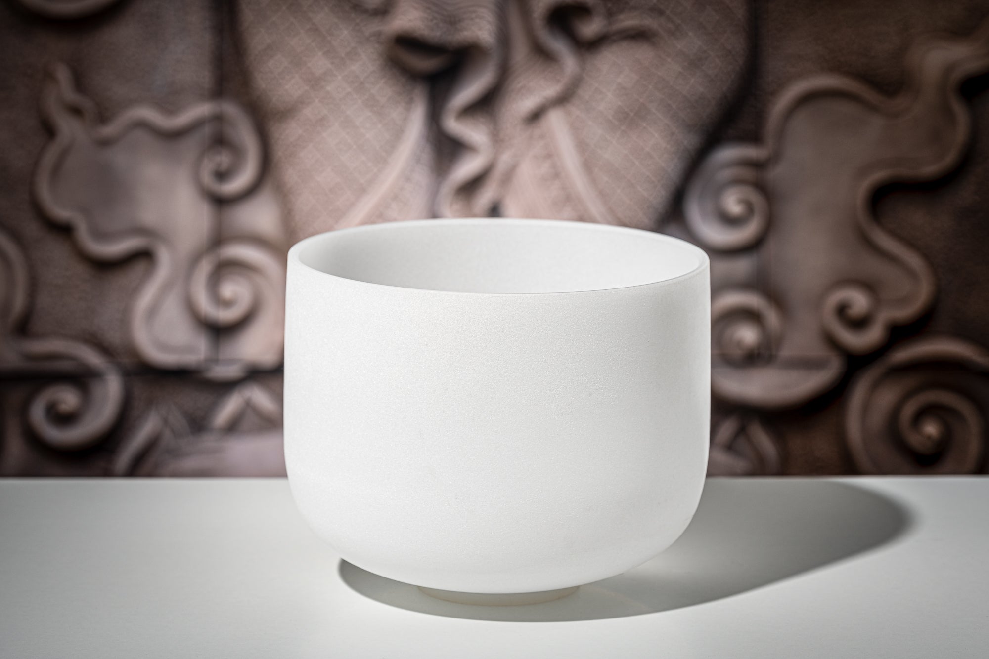 White frosted crystal singing bowl on reflective surface with textured brown background showing pure quartz quality