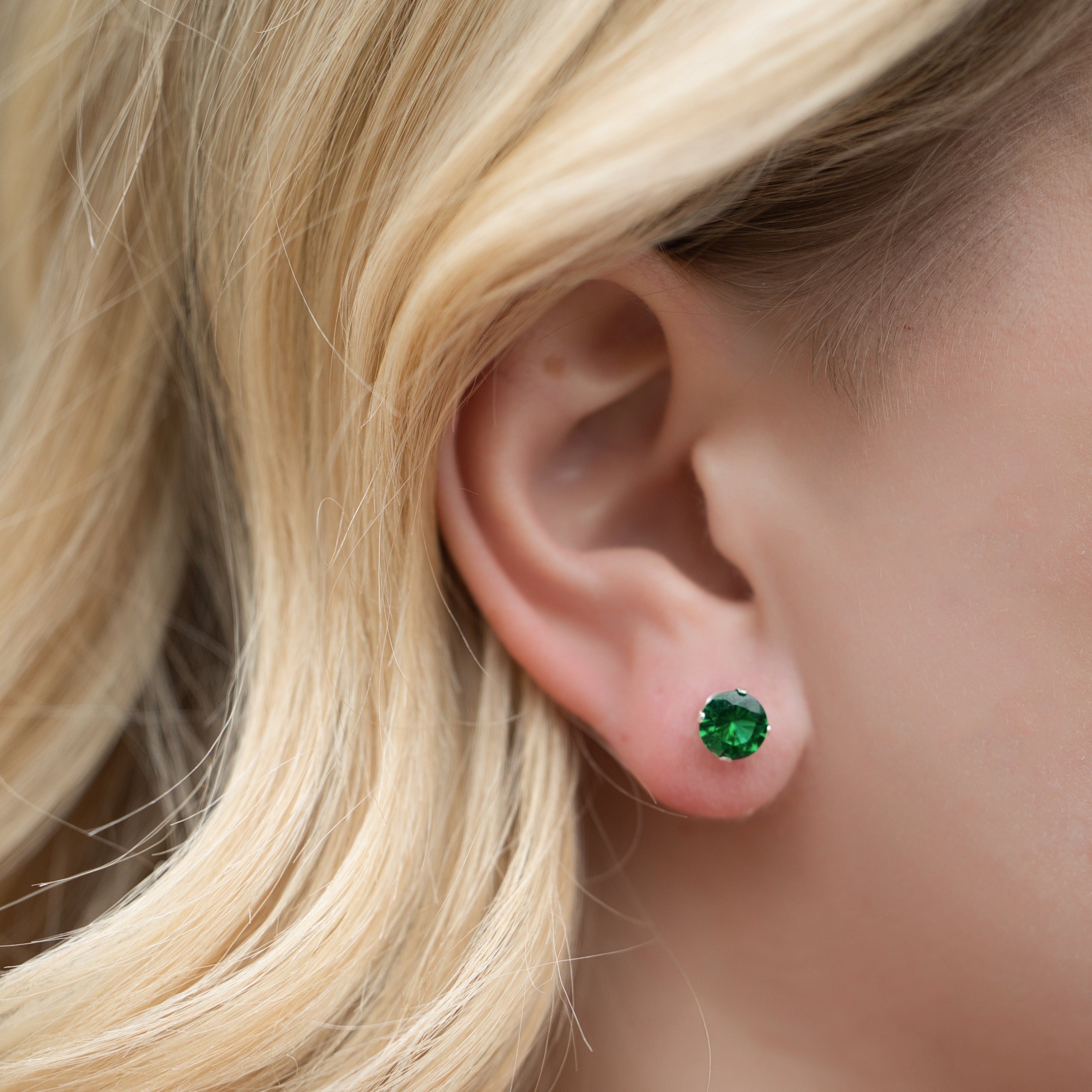 Close-up of an ear wearing a green gemstone earring with blonde hair.