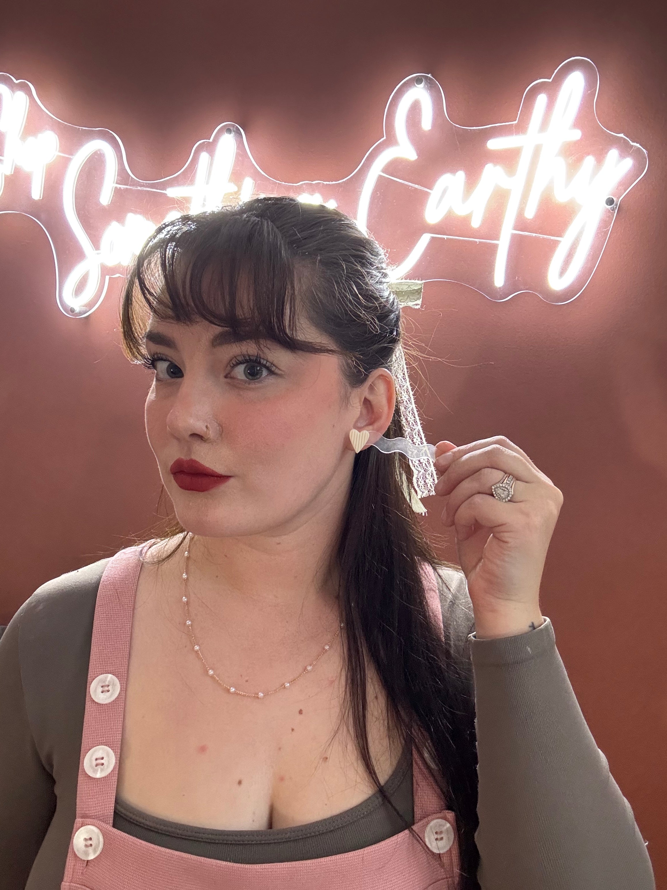 Woman wearing ivory ribbed heart stud earrings with neon sign background showing Valentine's Day gift jewelry