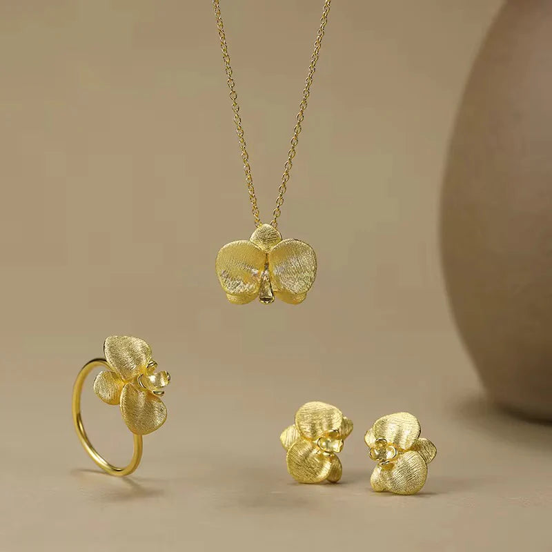 Gold orchid jewelry set with necklace, ring, and earrings on beige background - complete the set with matching pieces