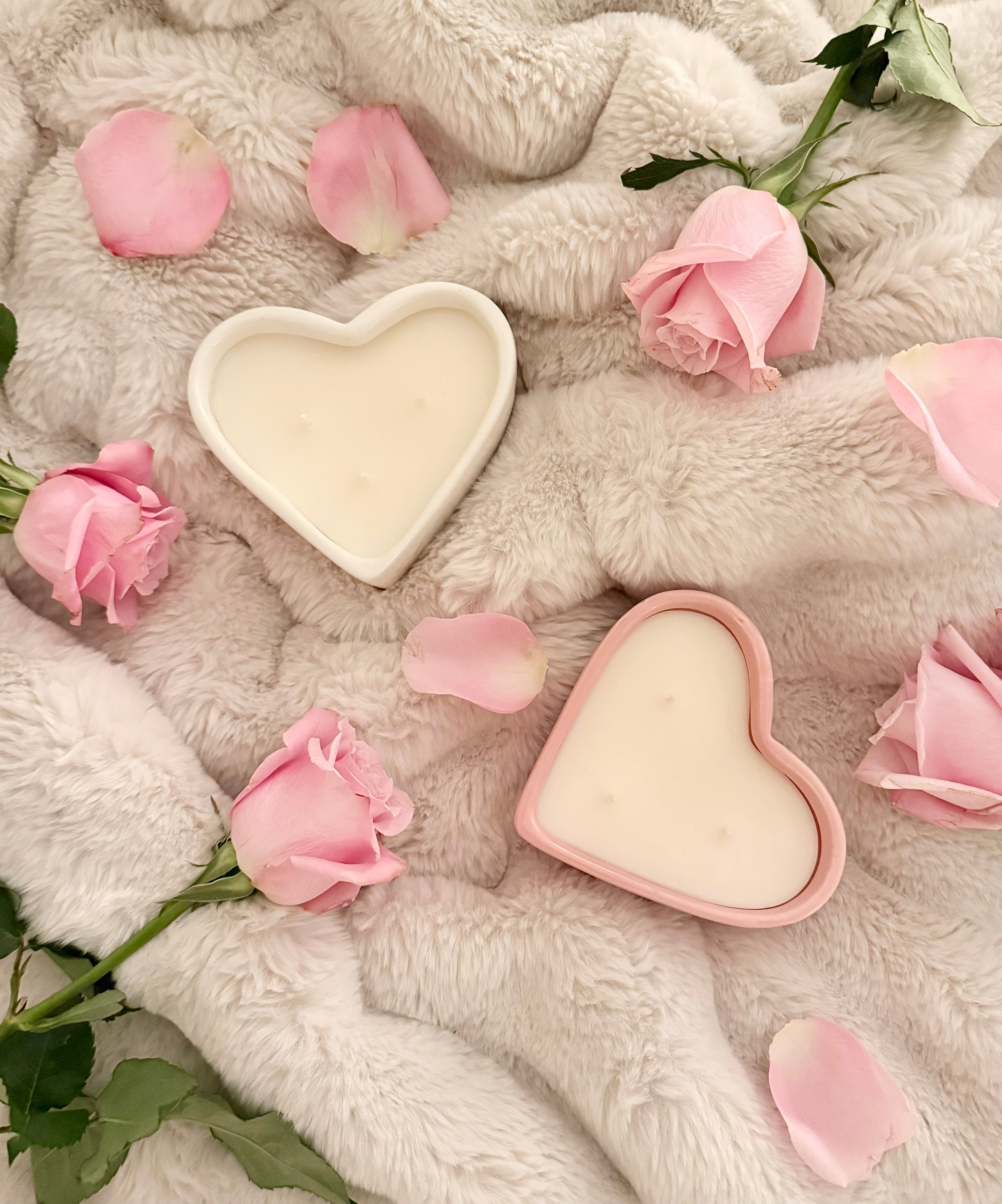 Pink and white heart-shaped candles on fluffy white blanket with scattered pink roses and petals - romantic Valentine's Day gift candle