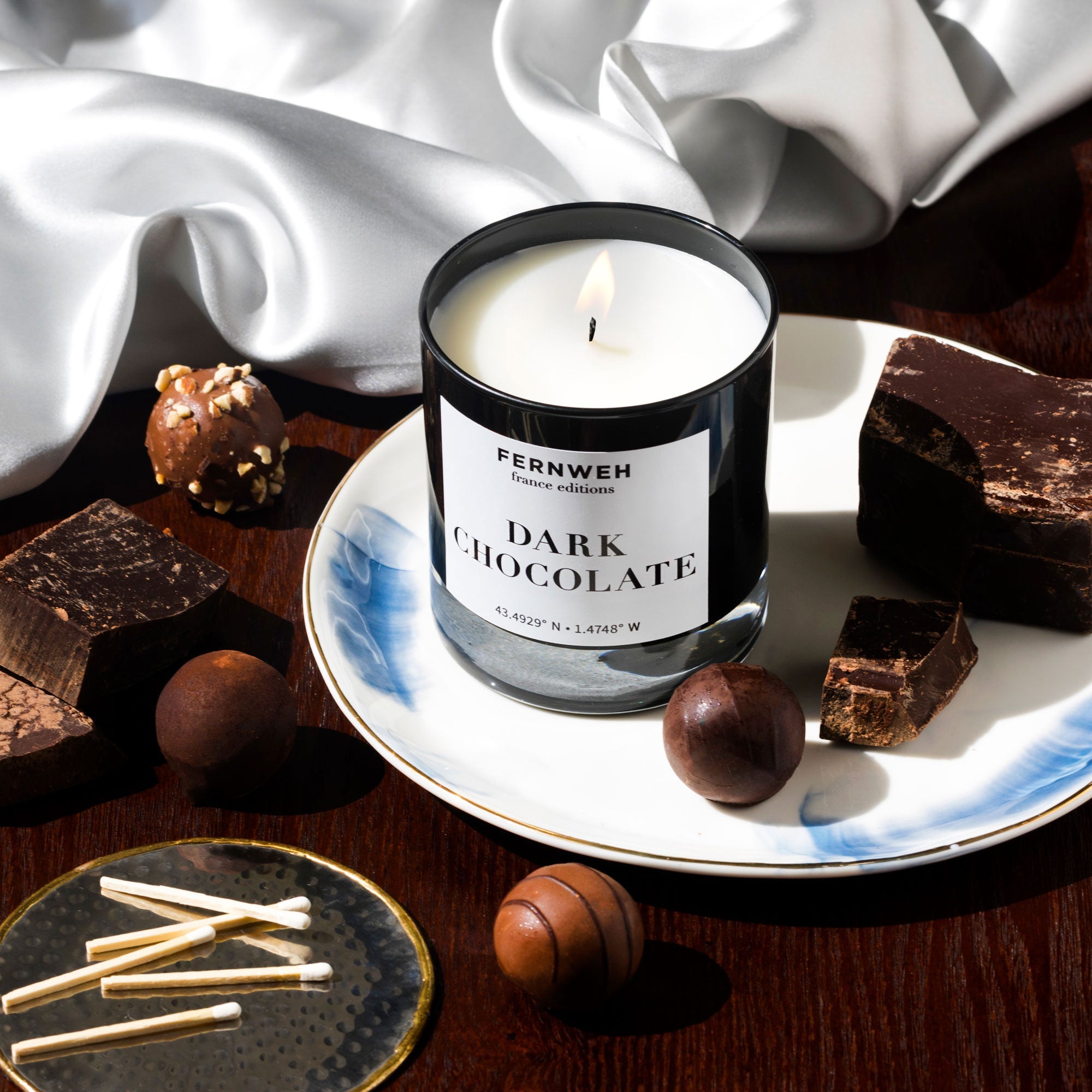 Fernweh Dark Chocolate scented candle in black jar on decorative plate with chocolate truffles and matches