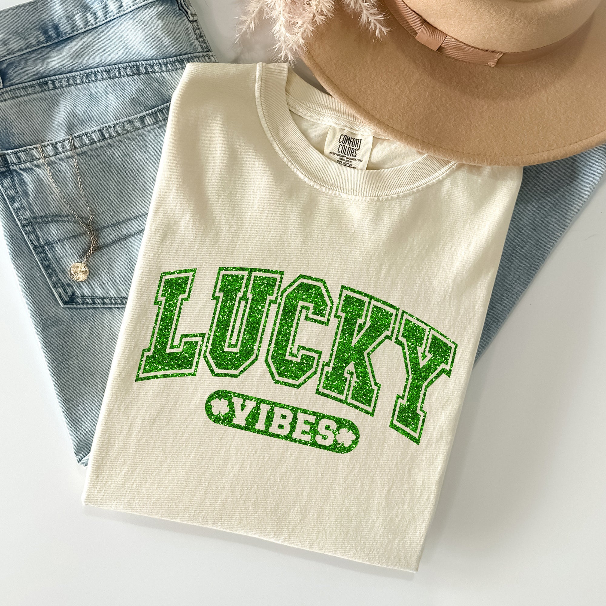 Lucky Vibes St. Patrick's Day t-shirt in Ivory with sparkly green text, styled with jeans and brown hat - retro vintage Comfort Colors tee
