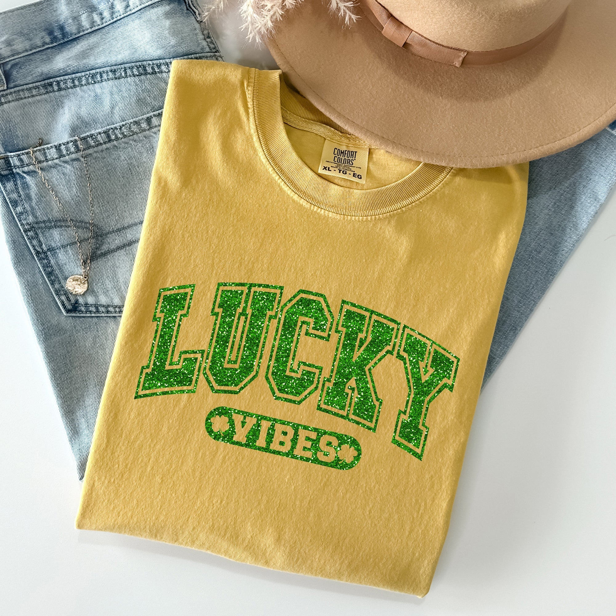 Lucky Vibes St. Patrick's Day t-shirt in Mustard yellow with sparkly green text, styled with denim and hat - vintage tee