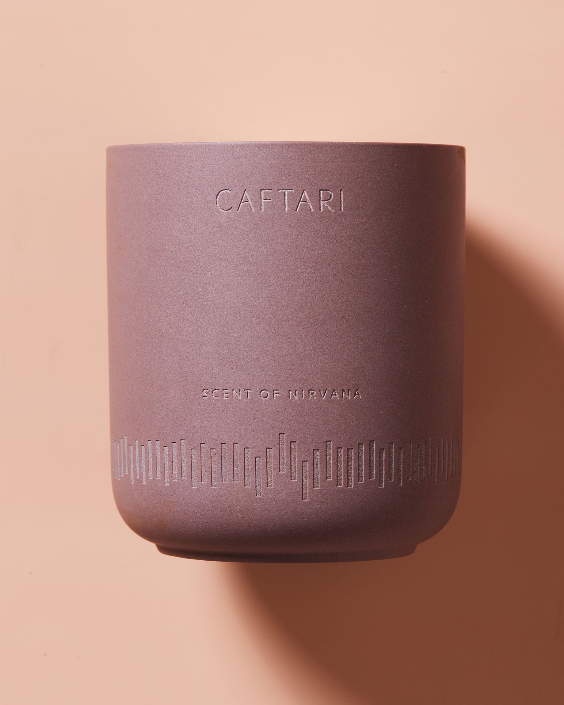 Scent of Nirvana meditation candle in rose-colored container with white wax and CAFTARI branding on peach background