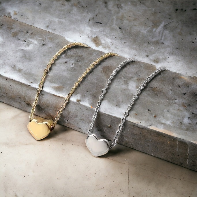 Close-up of waterproof gold and silver puffed heart anklets on concrete surface - stainless steel Valentine's Day jewelry