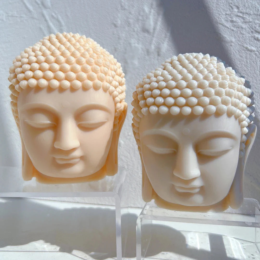 Close up of two light colored Buddha head candles on light gray background - handmade candles from silicone mold