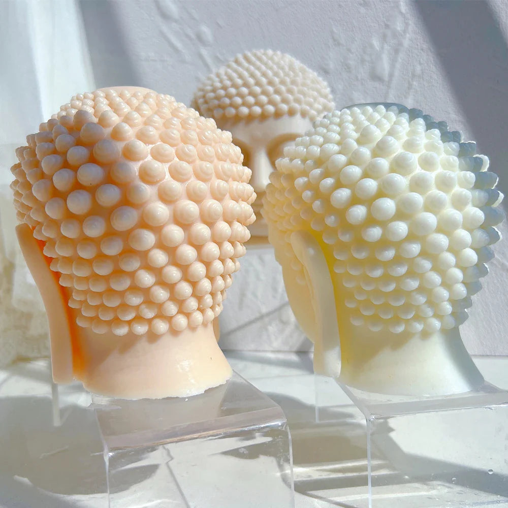 Back view close up of two light colored Buddha head candles on light gray background - Buddha candle details