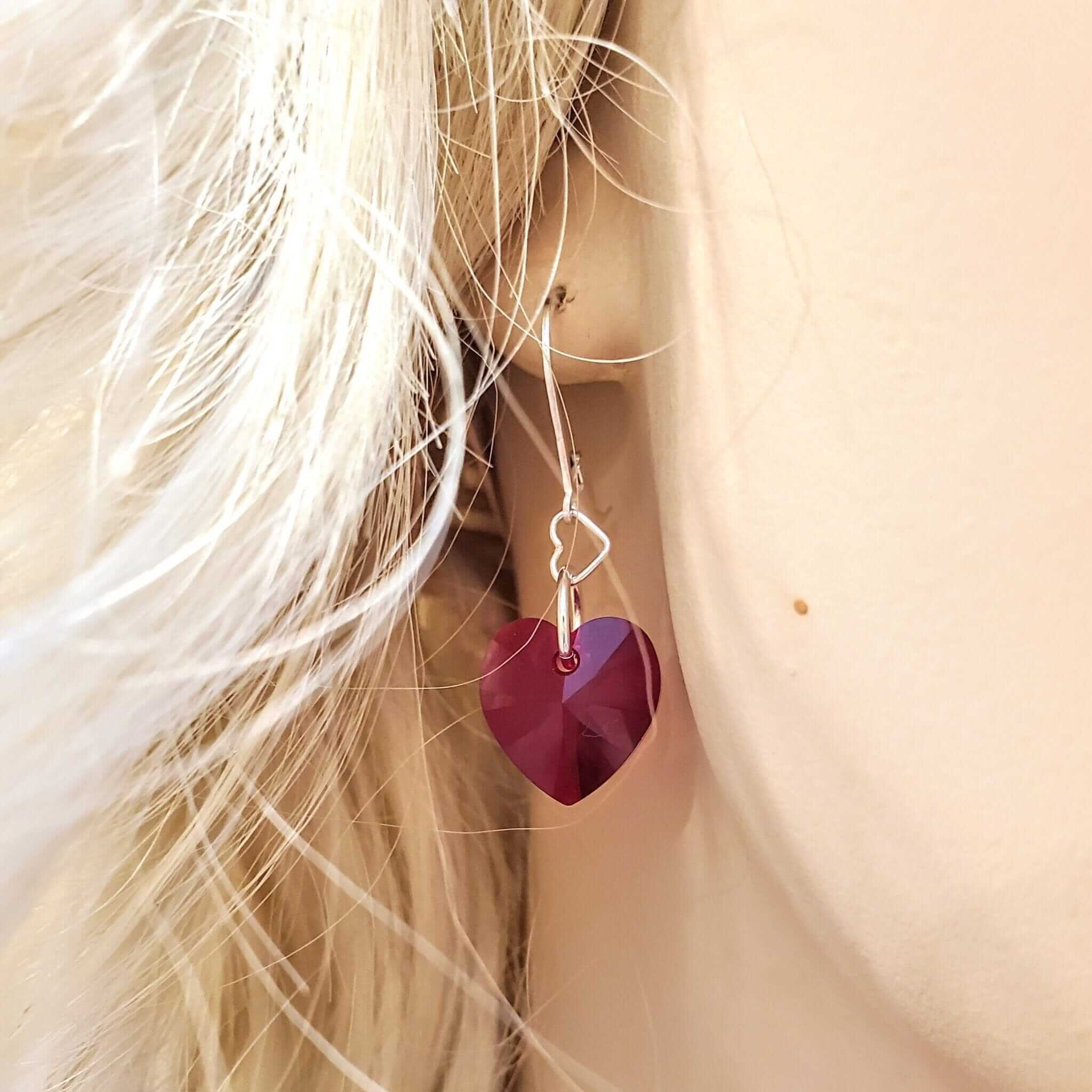 Close-up of woman wearing red heart-shaped Swarovski crystal earring with cross charm - Christian faith jewelry