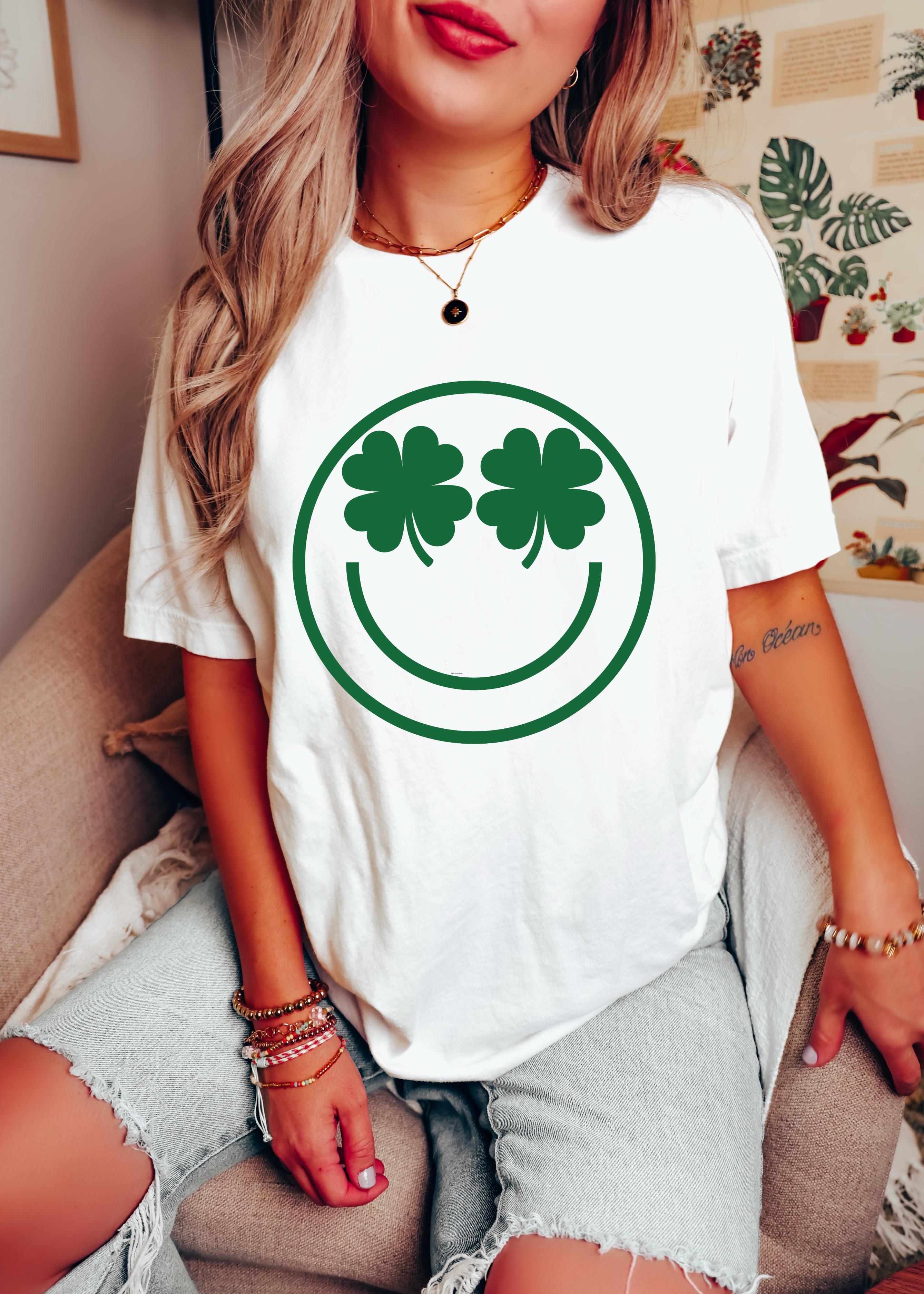 Person wearing a white t-shirt with a green shamrock smiley face design.