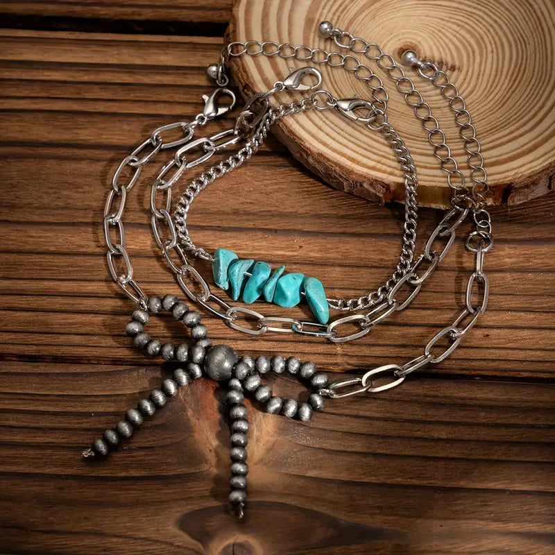 Stack of silver chain bracelets with turquoise stones and beaded bow on wooden surface - western boho jewelry set