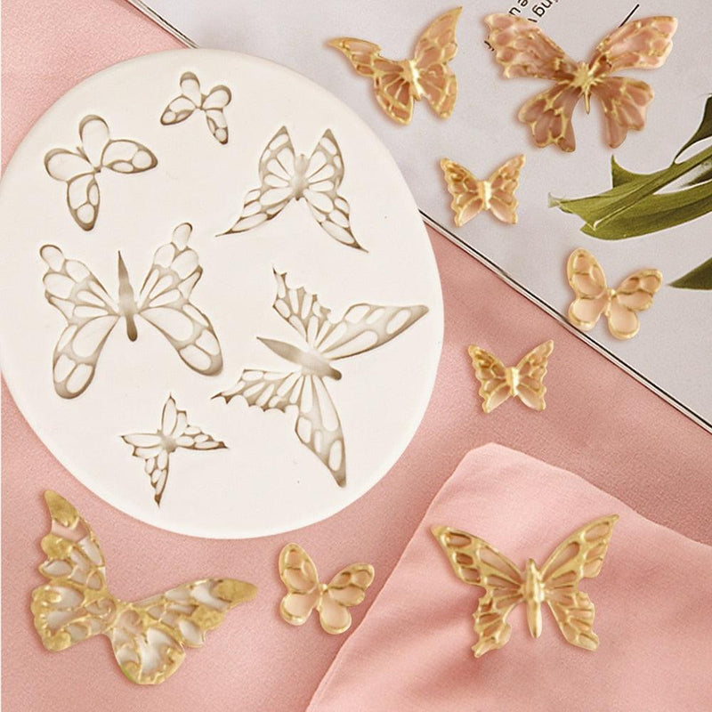 White silicone mold with various butterfly design cavities with gold epoxy resin butterfly decorations on a pink surface.