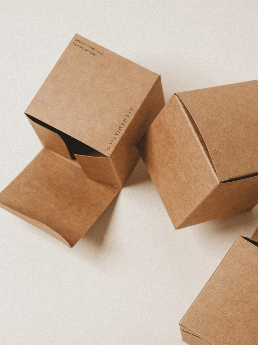 Brown paper Alchemist + Co. candle boxes on light beige background - wellness candle packaging