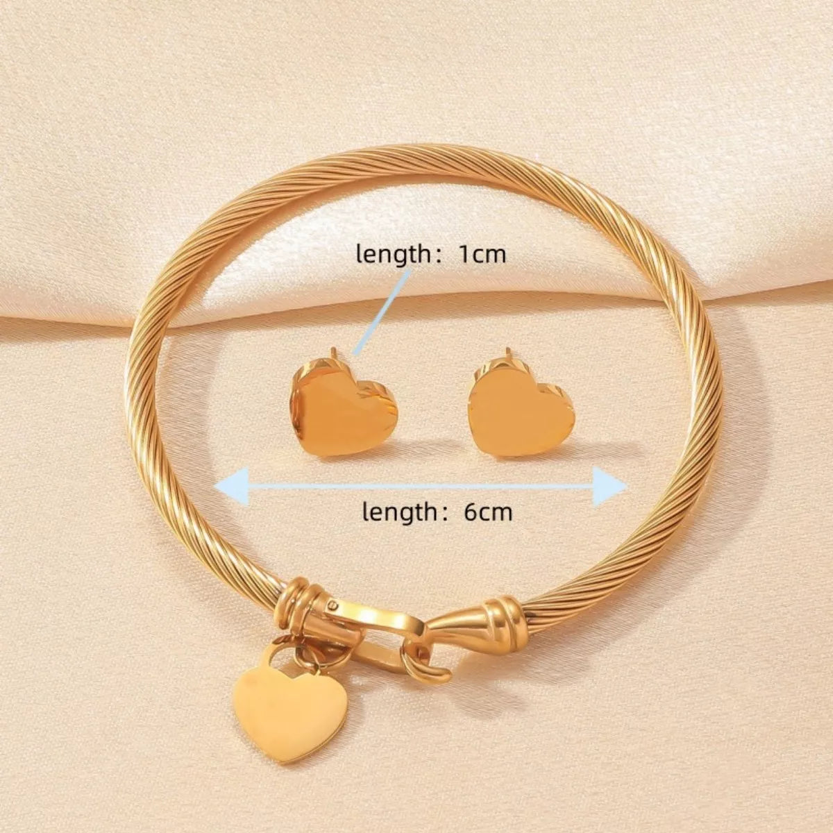 Gold bracelet and heart-shaped earrings on a beige background with measurements