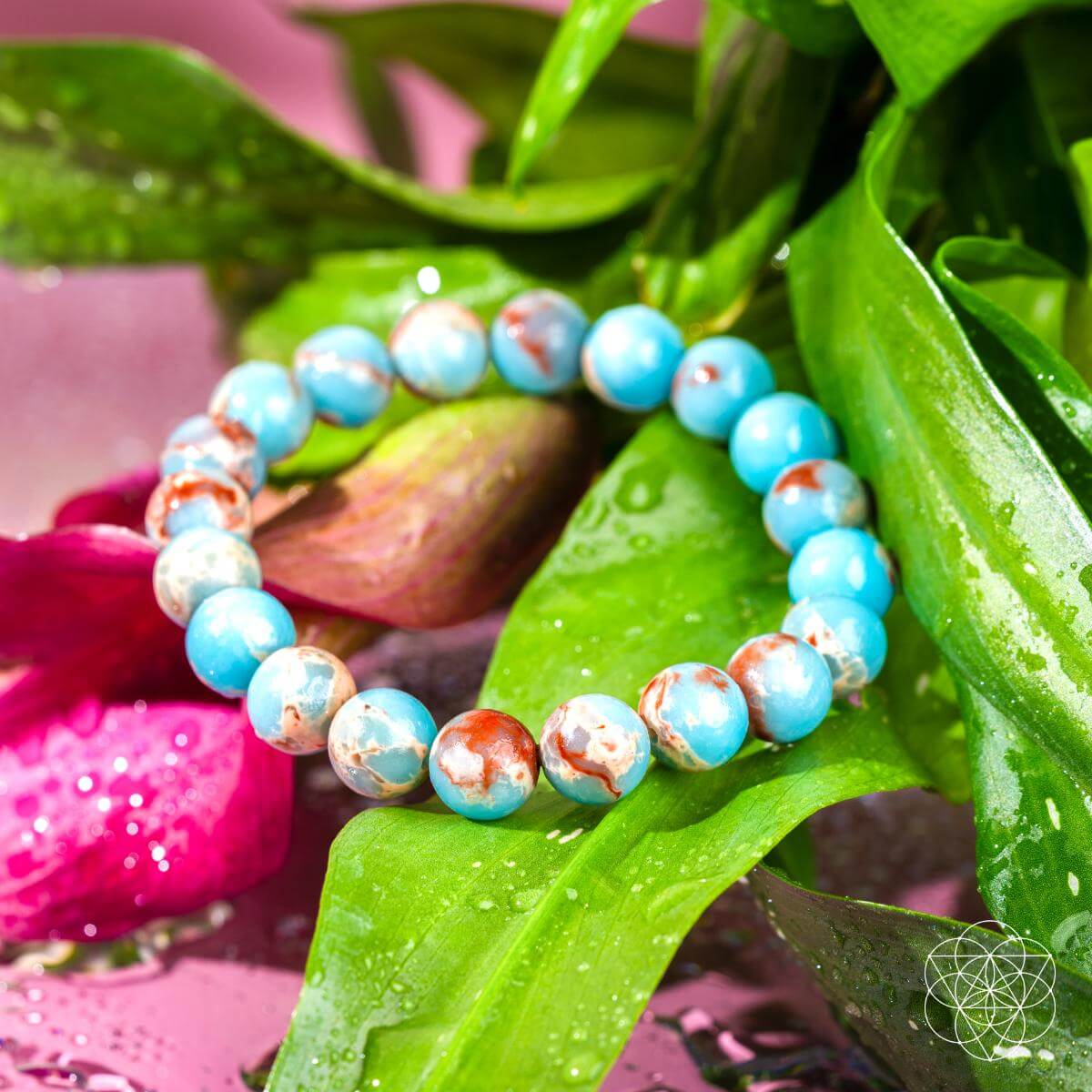 Multicolored aqua terra jasper beaded bracelet on leaf with pink flowers - closeup view
