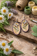 Hand-painted daisy oval earrings with purple edge on rustic wood background with flowers and paint jars - handmade floral dangle earrings