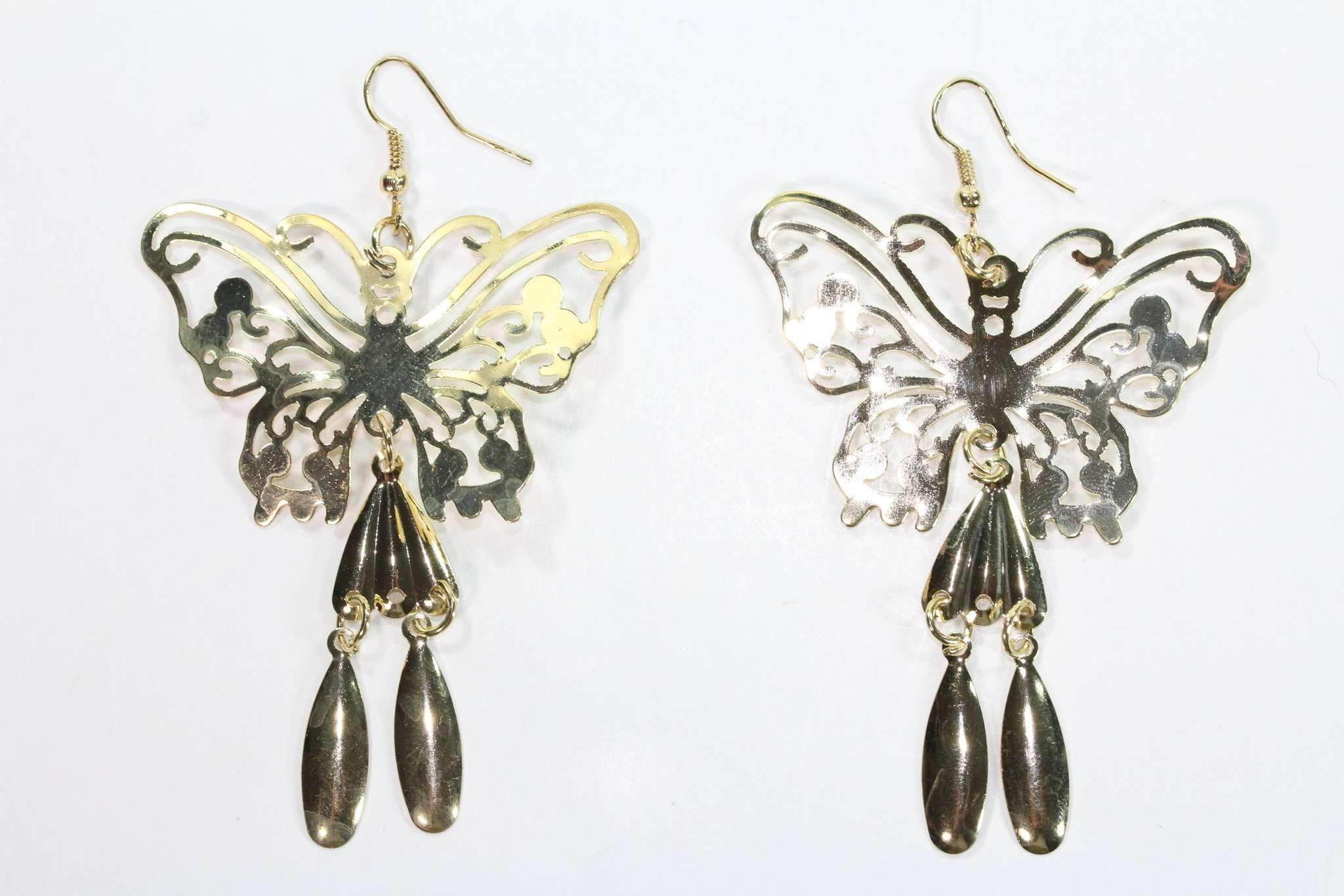 Closeup of butterfly-shaped filigree gold tone earrings with dangling elements on a white background