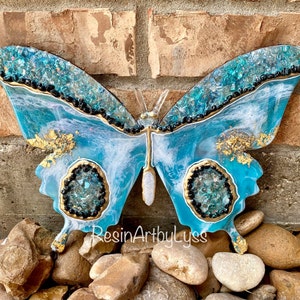 Decorative wooden butterfly decorated with resin and colorful paint with blue and gold details on a stone surface